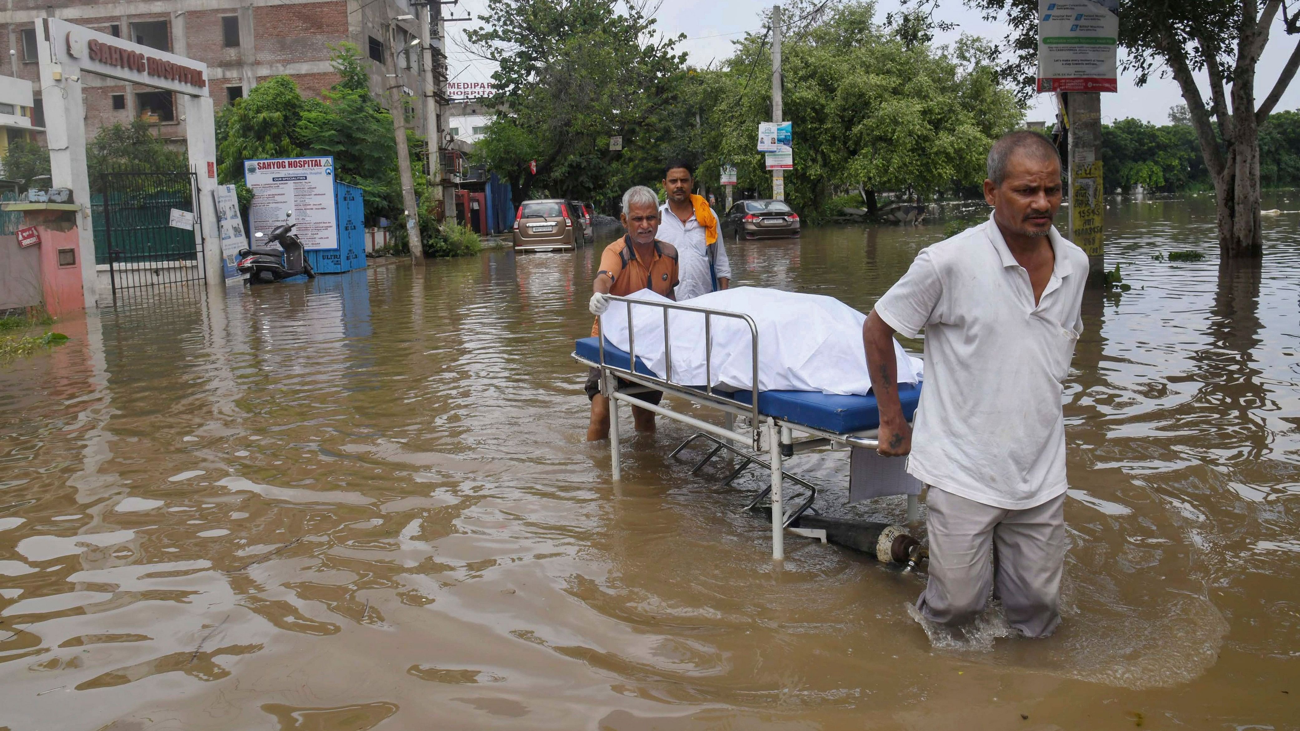 <div class="paragraphs"><p>Health workers wade through a waterlogged area near a hospital after heavy rainfall, in Patna, on Sunday</p></div>